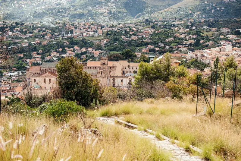 Monreale Cathedral and the town seen across dry grass from the hillside above, with the slopes of Monte Caputo rising behind
