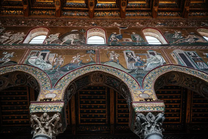 Pointed arches at Monreale springing from intricately carved stone capitals, framed by mosaic scenes and gilded ceiling beams