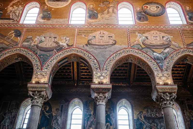 Two tiers of Old Testament mosaics on the nave wall of Monreale Cathedral showing Noah's Ark scenes above pointed arches on granite columns