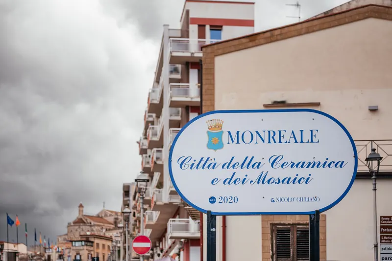 A road sign at the entrance to Monreale reading Città della Ceramica e dei Mosaici, with the cathedral towers in the distance